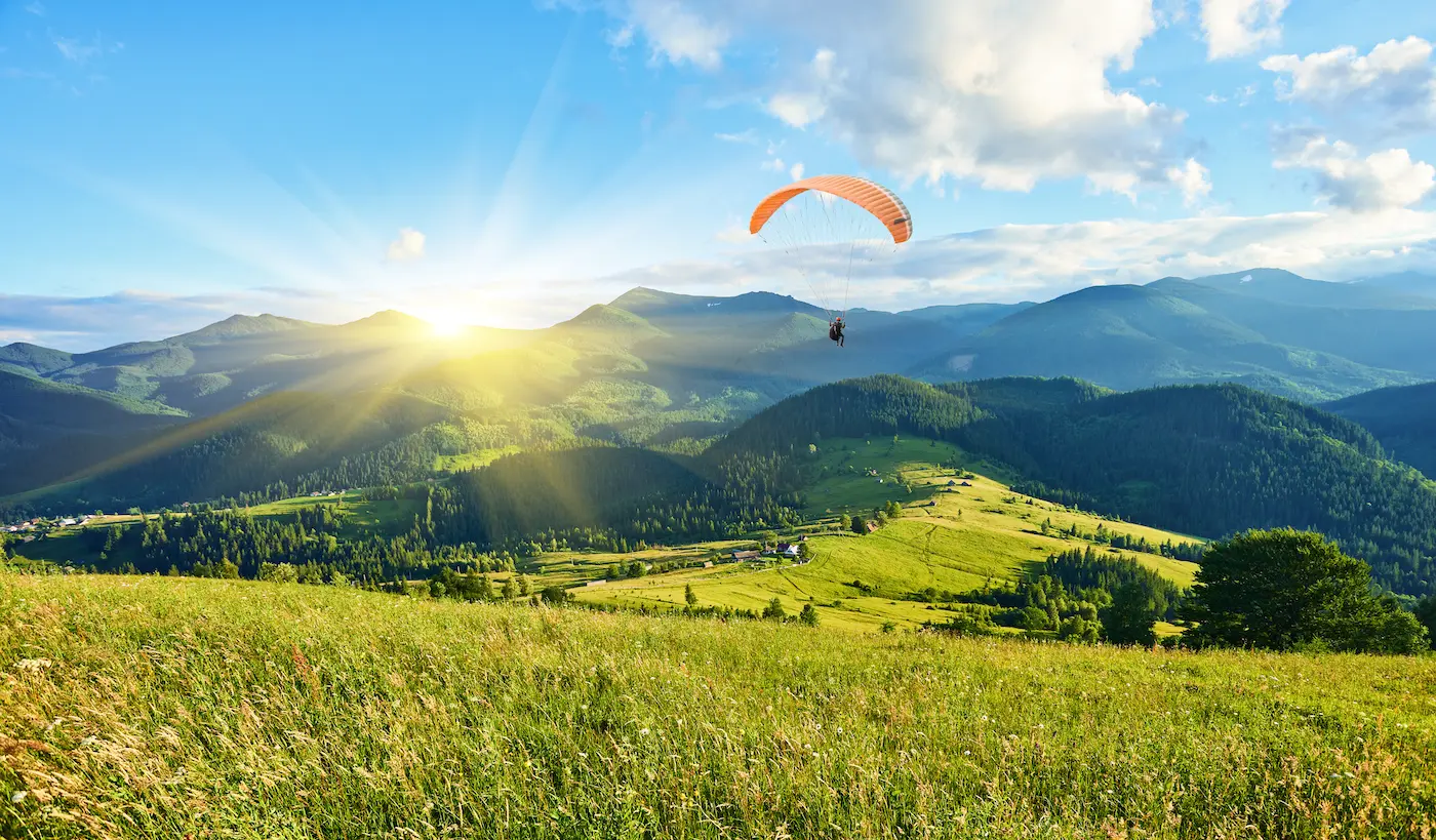 Paraglider flying over green hills and mountains in summer